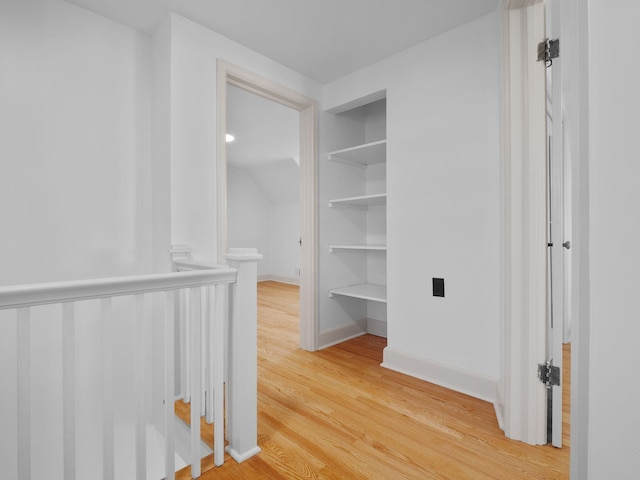 hallway featuring built in features, light wood-style floors, and baseboards
