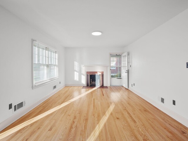 unfurnished living room with a brick fireplace, wood finished floors, and baseboards