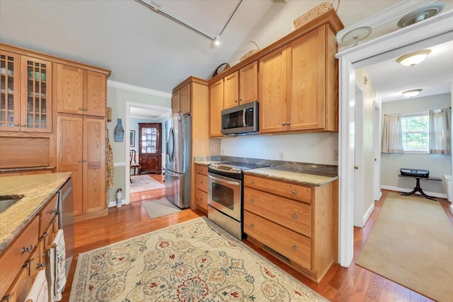 kitchen featuring stainless steel appliances, light wood-type flooring, light stone countertops, glass insert cabinets, and brown cabinetry
