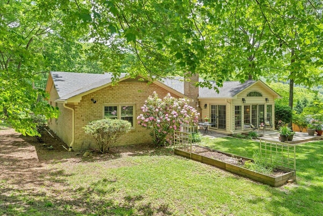 rear view of property with a garden, a yard, a chimney, brick siding, and a patio area