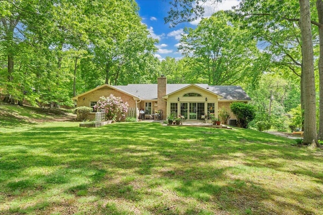rear view of property with a chimney, a yard, brick siding, and a patio