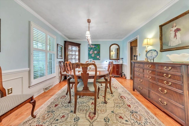 dining room with light wood-type flooring, crown molding, and a wainscoted wall
