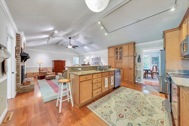 kitchen featuring rail lighting, stainless steel appliances, a breakfast bar area, a sink, and light wood-style floors