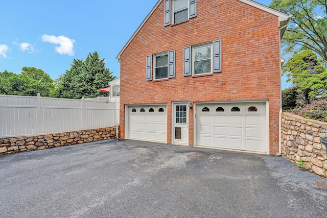 view of home's exterior with asphalt driveway, an attached garage, fence, and brick siding