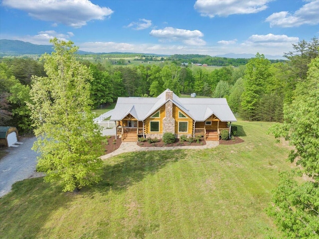 view of front of property with a porch, stone siding, a chimney, metal roof, and a view of trees