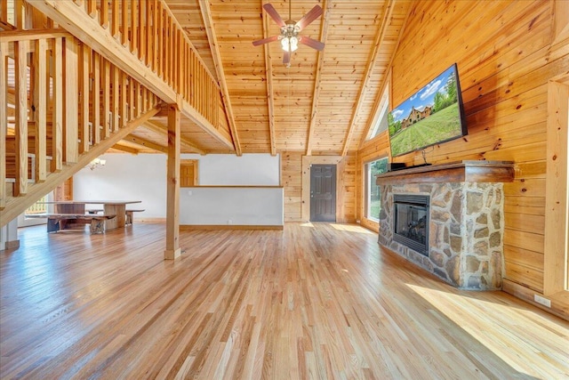 unfurnished living room featuring wood finished floors, healthy amount of natural light, a stone fireplace, a high ceiling, and wooden walls