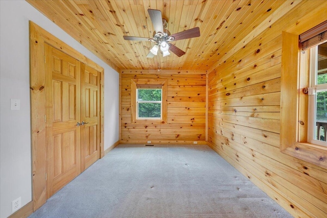 additional living space with carpet, wood ceiling, wooden walls, and a ceiling fan