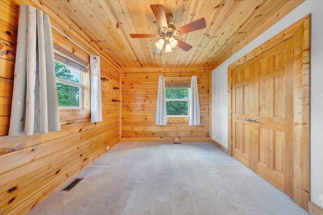 carpeted spare room with wood walls, wood ceiling, and ceiling fan