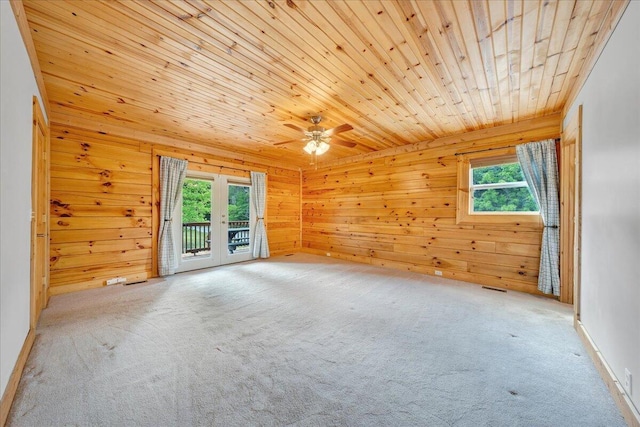 carpeted empty room featuring healthy amount of natural light, wood walls, wooden ceiling, and ceiling fan