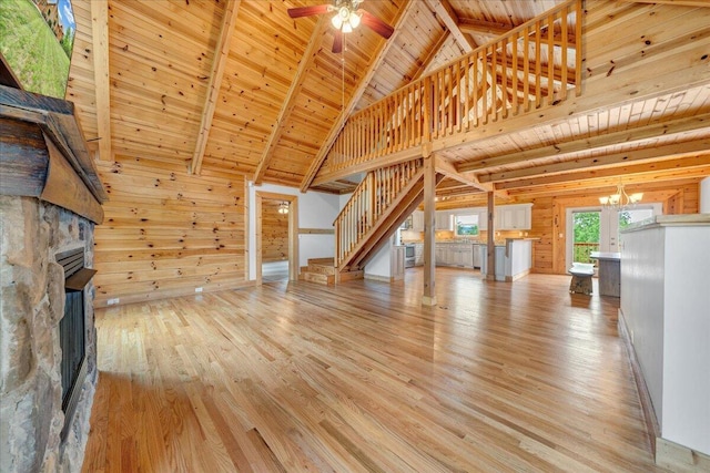 unfurnished living room with stairway, wooden ceiling, beam ceiling, light wood-style floors, and wood walls