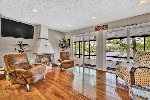 living area with healthy amount of natural light, a textured ceiling, hardwood / wood-style floors, a large fireplace, and recessed lighting