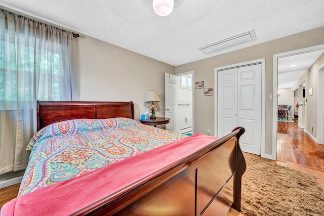 bedroom with multiple windows, a closet, light wood finished floors, and a baseboard radiator