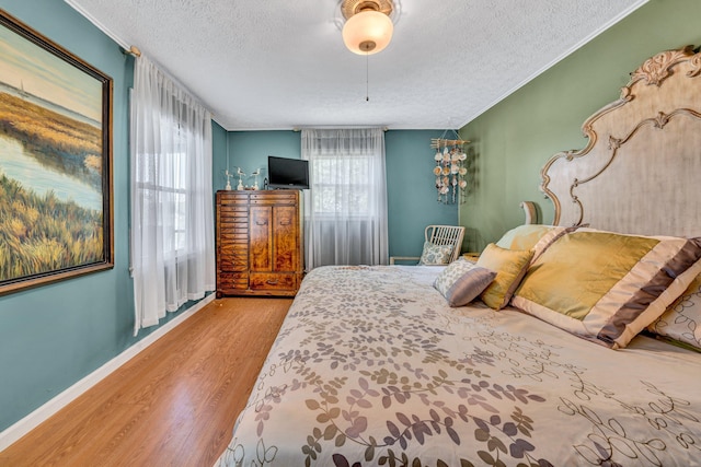 bedroom featuring a textured ceiling, wood finished floors, multiple windows, and baseboards