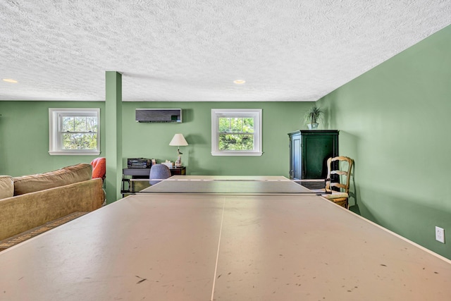 rec room with a wall mounted air conditioner, plenty of natural light, a textured ceiling, and recessed lighting