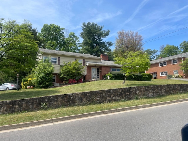 split level home with a chimney, a front yard, and brick siding