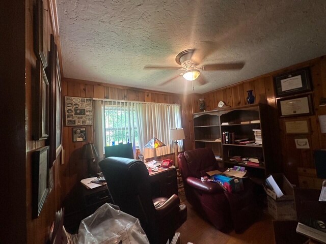 office area with a ceiling fan, wooden walls, a textured ceiling, and wood finished floors