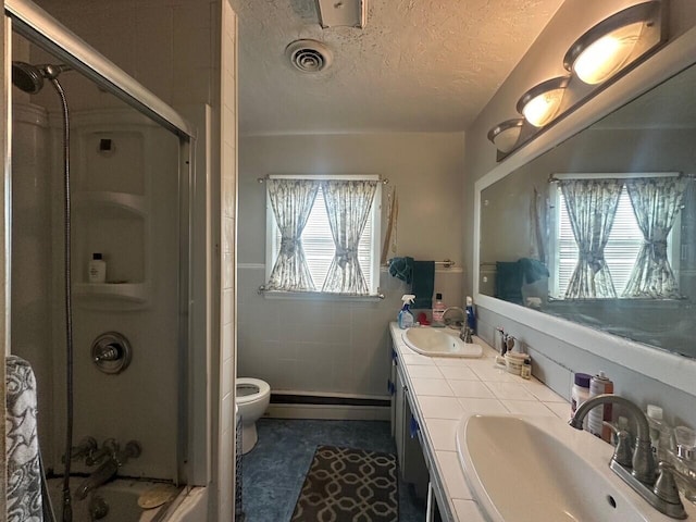 bathroom featuring a shower with door, a textured ceiling, a baseboard heating unit, double vanity, and toilet