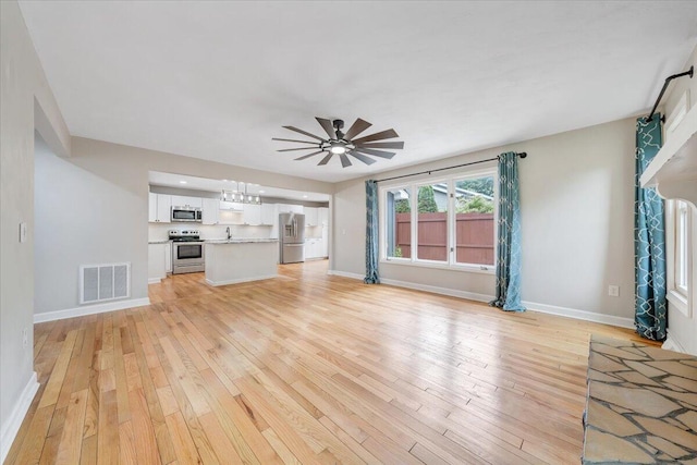 unfurnished living room featuring light wood finished floors, baseboards, a chandelier, and ceiling fan