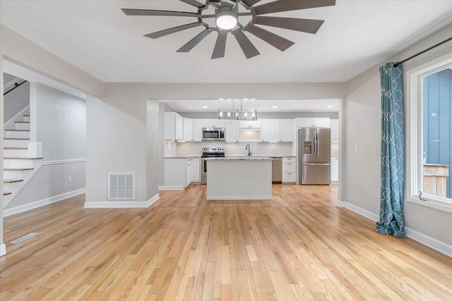 unfurnished living room with light wood-style flooring, stairway, ceiling fan, baseboards, and a sink