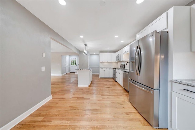kitchen with appliances with stainless steel finishes, a kitchen island, white cabinetry, light wood-type flooring, and baseboards