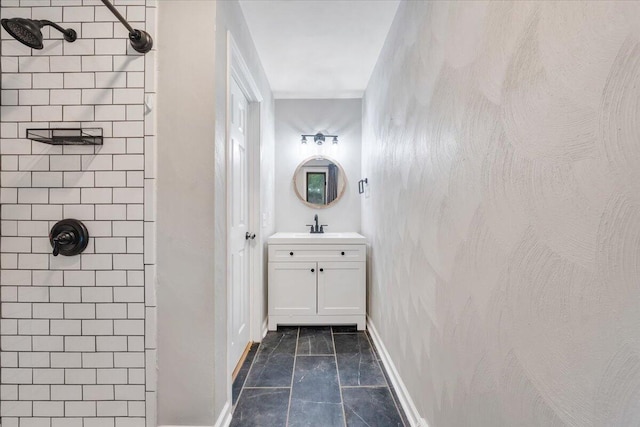 bathroom with a tile shower, vanity, baseboards, and marble look tile flooring