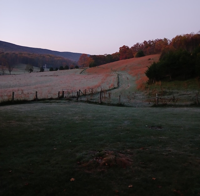 yard at dusk featuring a rural view, a mountain view, and a yard