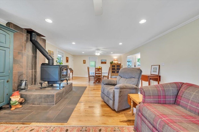living room with a wood stove, ornamental molding, ceiling fan, recessed lighting, and light wood-style floors