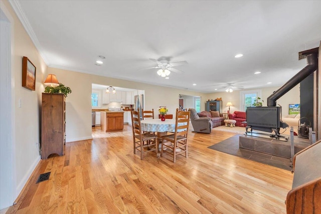 dining space featuring a wood stove, a ceiling fan, ornamental molding, light wood-type flooring, and recessed lighting
