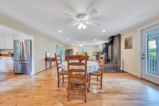dining space featuring crown molding, healthy amount of natural light, a ceiling fan, a wood stove, and light wood-style flooring