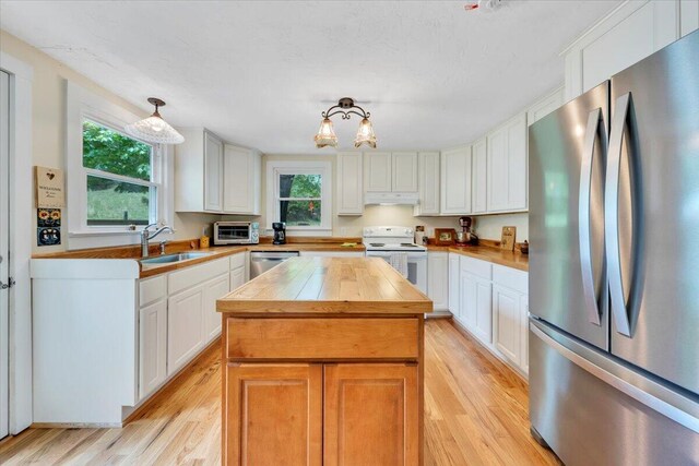 kitchen with appliances with stainless steel finishes, butcher block countertops, under cabinet range hood, and light wood-type flooring
