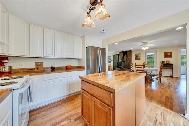 kitchen featuring wooden counters, freestanding refrigerator, white range with electric stovetop, a wood stove, and light wood-style flooring