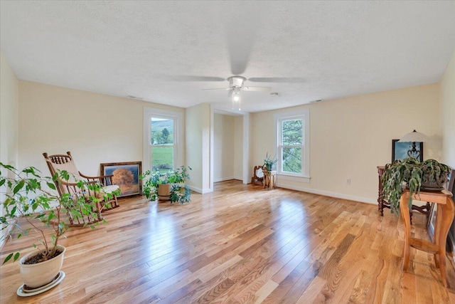 sitting room with light wood-style flooring, a ceiling fan, a textured ceiling, and baseboards