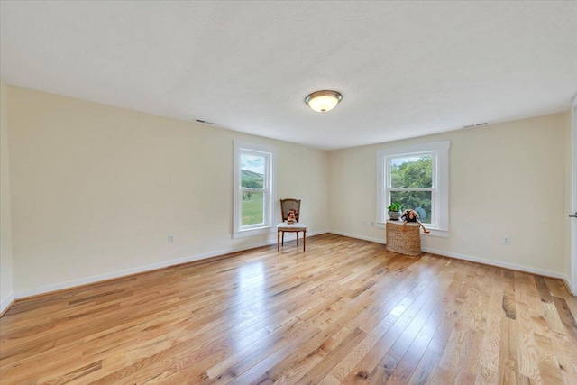 empty room with healthy amount of natural light, light wood-style flooring, and baseboards