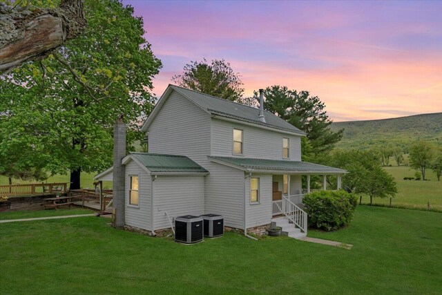 back of house at dusk featuring metal roof, a porch, central AC unit, and a lawn