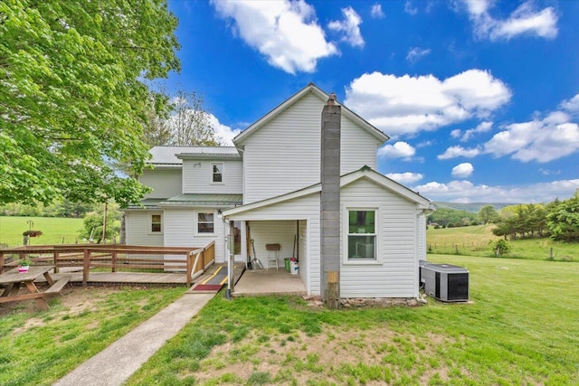 back of house with central AC unit, a patio, a lawn, and metal roof