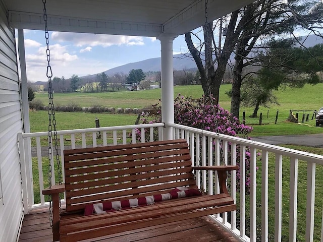 wooden deck with a porch, a mountain view, a yard, and a rural view