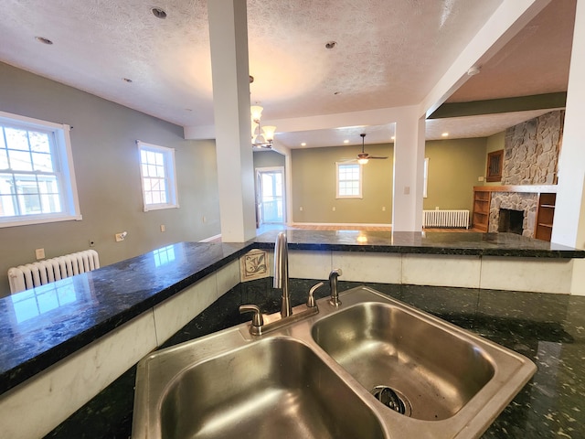 kitchen with radiator heating unit, a sink, open floor plan, a textured ceiling, and a fireplace