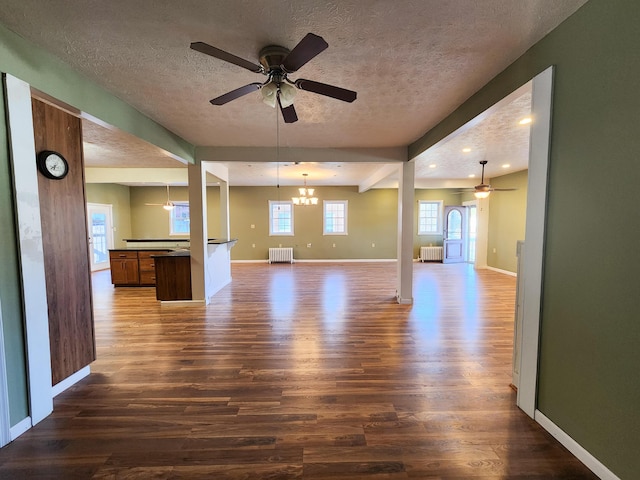 unfurnished living room featuring a ceiling fan, dark wood-style floors, a textured ceiling, a chandelier, and radiator heating unit