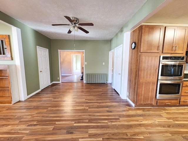 kitchen with stainless steel double oven, radiator, wood finished floors, ceiling fan, and baseboards