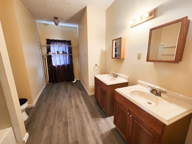 full bath with wood finished floors, two vanities, and baseboards