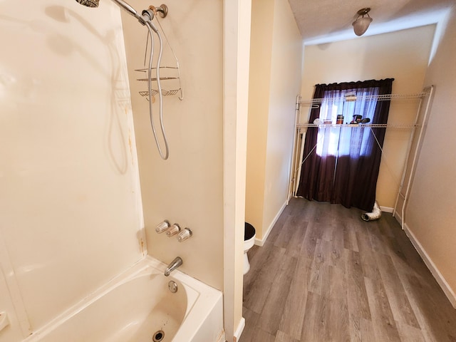bathroom with wood finished floors, bathtub / shower combination, toilet, and baseboards