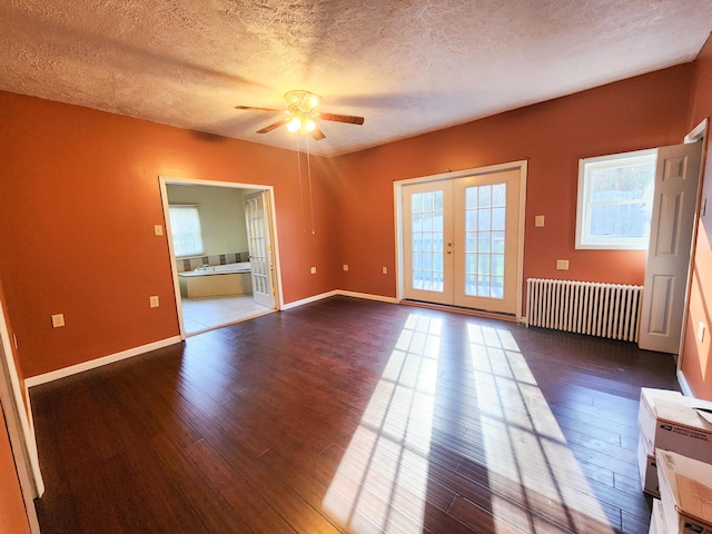 empty room featuring radiator heating unit, dark wood-type flooring, ceiling fan, a textured ceiling, and french doors