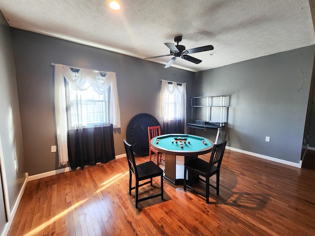 rec room with hardwood / wood-style floors, a textured ceiling, a ceiling fan, and baseboards