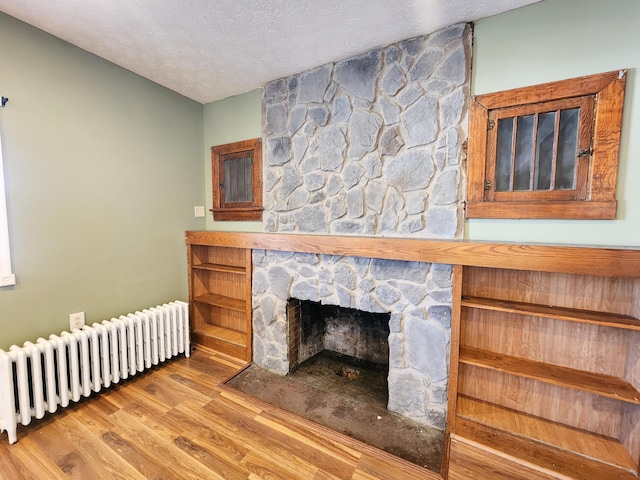 living area featuring radiator, wood finished floors, a fireplace, and a textured ceiling