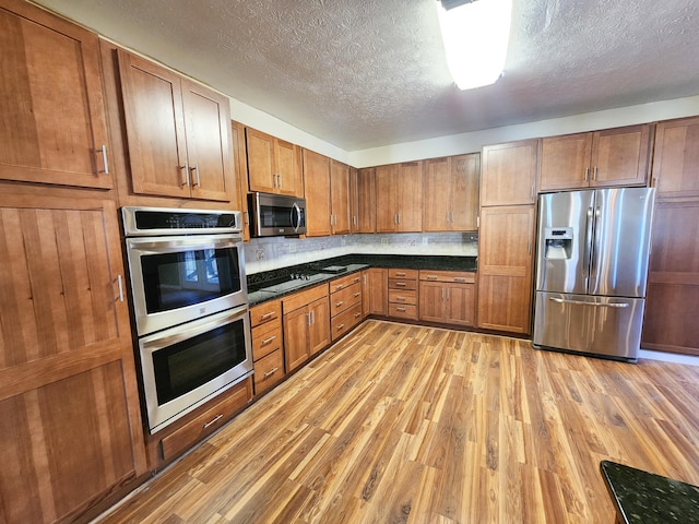 kitchen featuring stainless steel appliances, a textured ceiling, light wood-style flooring, brown cabinets, and dark countertops