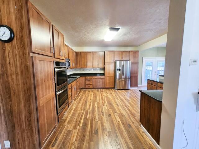kitchen with appliances with stainless steel finishes, dark countertops, light wood-type flooring, a textured ceiling, and brown cabinetry