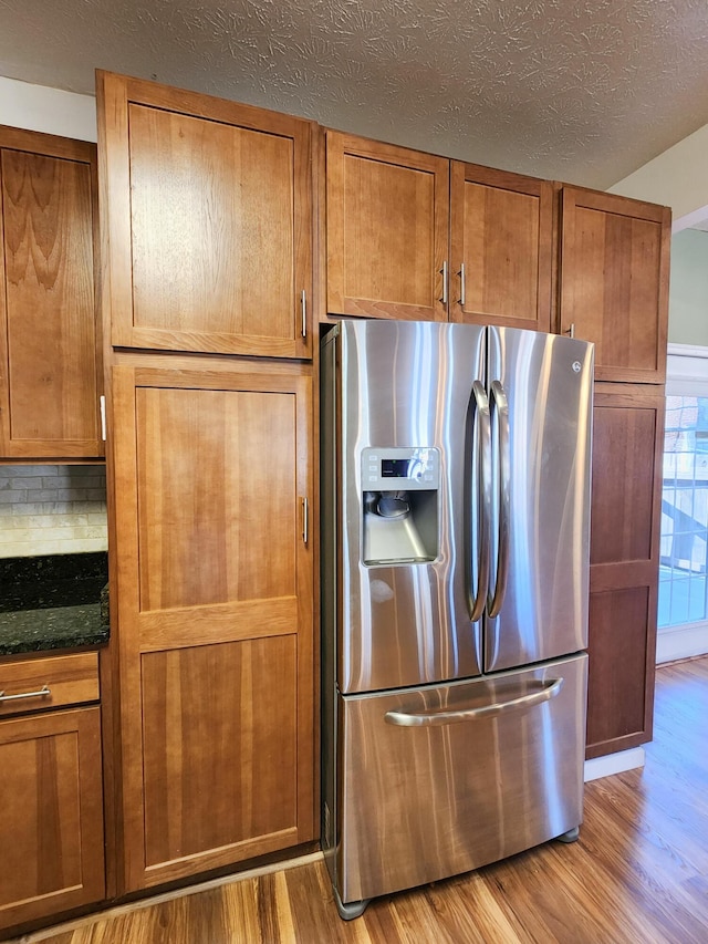 kitchen featuring stainless steel fridge, wood finished floors, brown cabinets, a textured ceiling, and backsplash