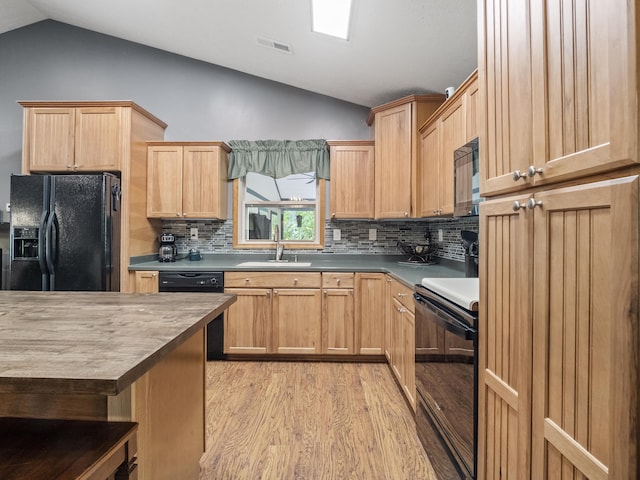 kitchen with black appliances, vaulted ceiling, a sink, light wood-style floors, and decorative backsplash