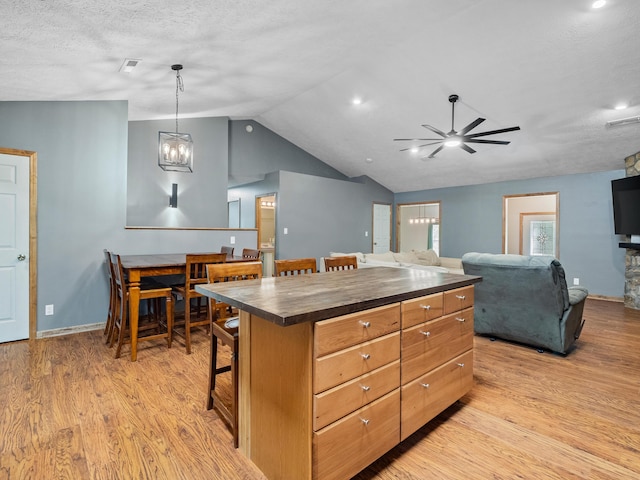 kitchen with lofted ceiling, ceiling fan, light wood-style floors, a kitchen bar, and open floor plan