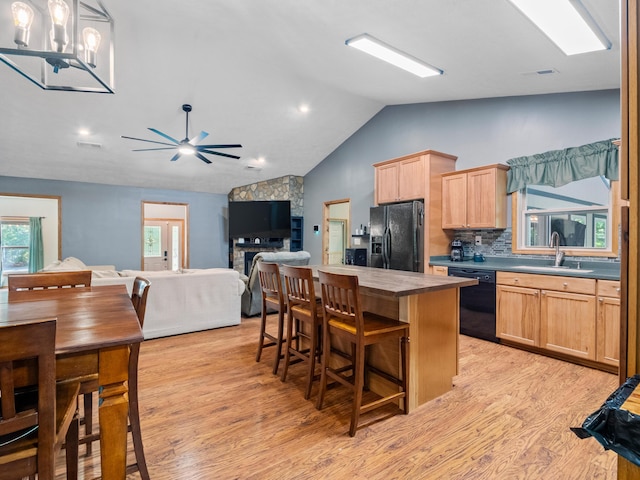 kitchen featuring black appliances, light brown cabinets, lofted ceiling, light wood-style flooring, and a sink
